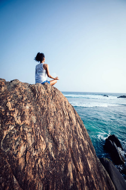 Young woman in white clothing  meditating at the seaside cliff edge - Foto, immagini