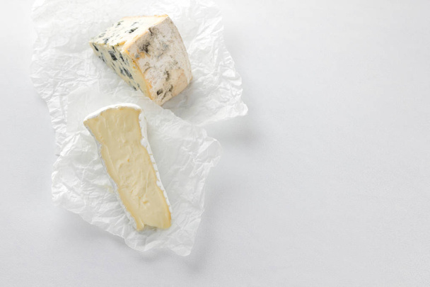 Camembert ja sinihomejuusto pergamenttipaperilla. Paloja eri juustoa valkoisella pohjalla. Dorblu ja pehmeä juusto minimalismin tyyliin. Ympäristöystävälliset maitotuotteet
 - Valokuva, kuva