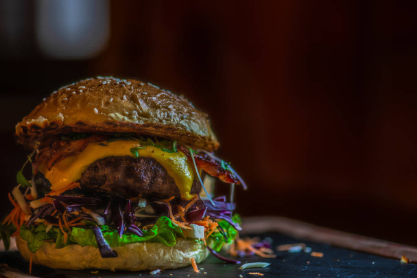 Typical american hamburger with meat, cheese and different vegetables on dark rustic background with copy space - Photo, Image