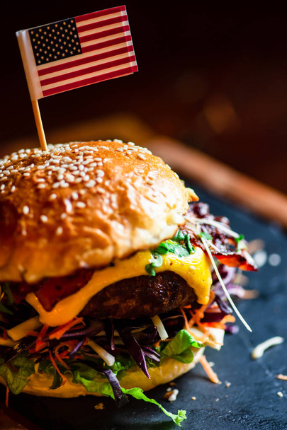 Typische Amerikaanse hamburger met vlees, kaas en verschillende groenten op donkere rustieke achtergrond met kopie ruimte - Foto, afbeelding