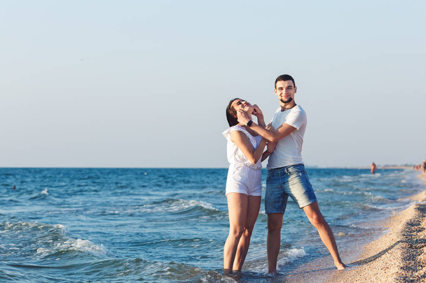 ο άνθρωπος εκτείνεται αστείο πρόσωπο μιας γυναίκας με τα χέρια του. νεαρό ζευγάρι έχει τη διασκέδαση στην ακτή της θάλασσας. - Φωτογραφία, εικόνα