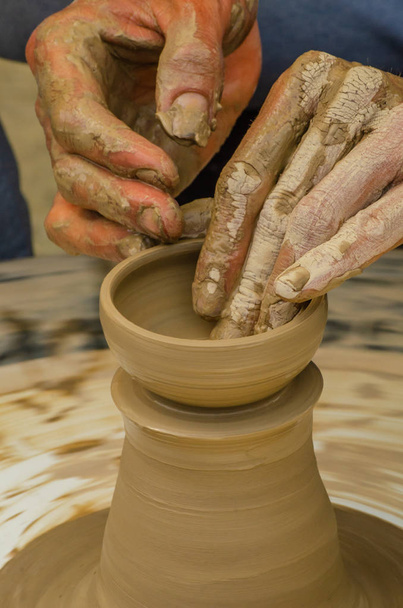 Close-up van de handen van de kunstenaar een klei pot, de traditionele methode van het creëren van keramische producten, hobby's maken - Foto, afbeelding