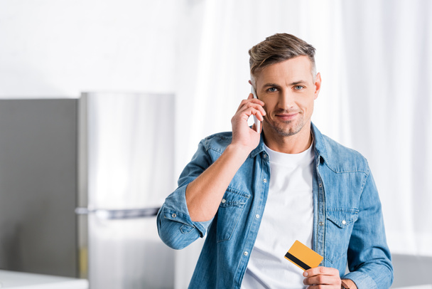 smiling man talking on smartphone and holding credit card  - Фото, зображення