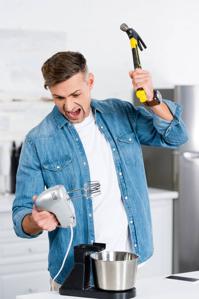 agresivo hombre adulto gritando mientras sostiene mezclador y martillo
  - Foto, imagen