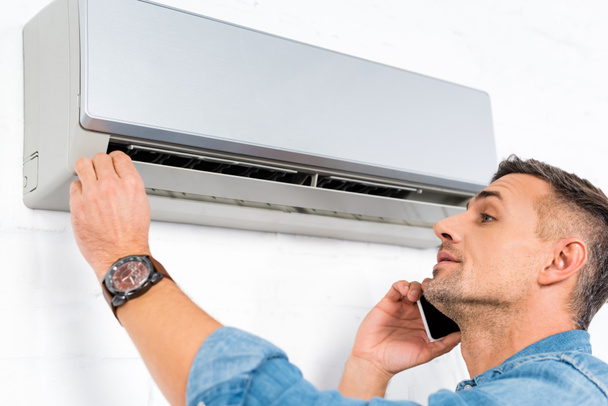 handsome man talking on smartphone while checking air conditioner  - Foto, Bild