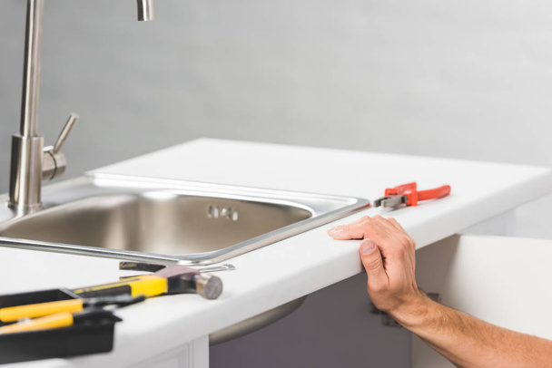 vista ritagliata di mano maschile appoggiata sul bancone della cucina con rubinetto vicino agli strumenti
 - Foto, immagini