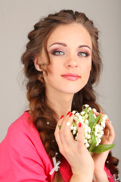 Young woman with beautiful hairstyle and flowers, on grey background - Fotoğraf, Görsel