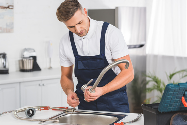 Nachdenklicher erwachsener Reparateur nimmt Küchenarmatur zur Reparatur ab  - Foto, Bild