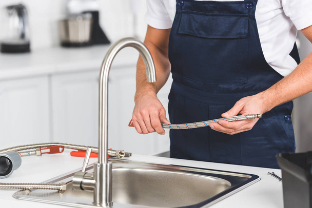 cropped view of repairman holding pipe in hands while repairing kitchen faucet  - Foto, Imagen