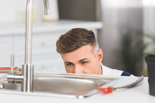 cropped view of adult repairman looking at sink at kitchen - Foto, immagini