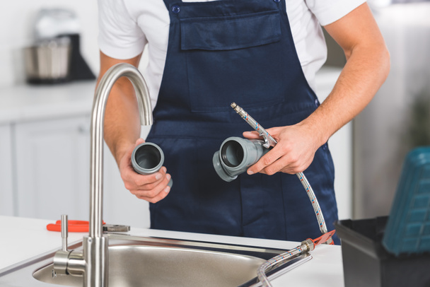 обрізаний вид ремонтника, що тримає труби та інструменти під час ремонту крана на кухні
  - Фото, зображення