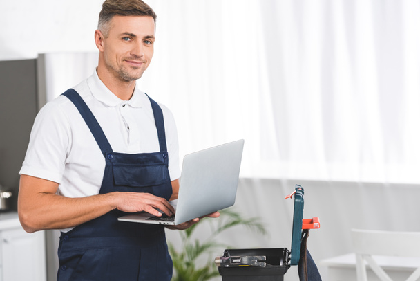 adult repairman holding laptop while standing at kitchen and looking at camera - Fotoğraf, Görsel