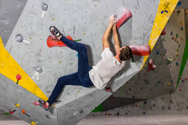 Rock climber man hanging on a bouldering climbing wall, inside on colored hooks - 写真・画像
