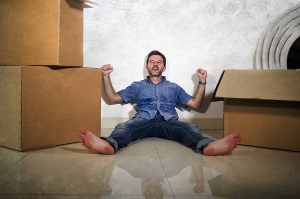 young happy and excited man at home floor enjoying unpacking cardboard boxes moving alone to new apartment or house smiling cheerful celebrating property owner status - Fotó, kép