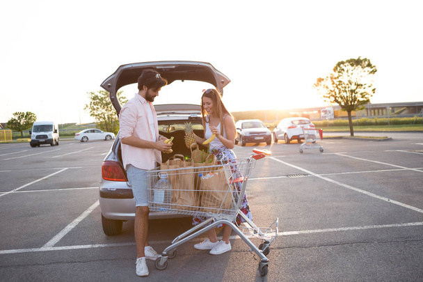 Un couple heureux met des courses dans sa voiture devant un supermarché
. - Photo, image