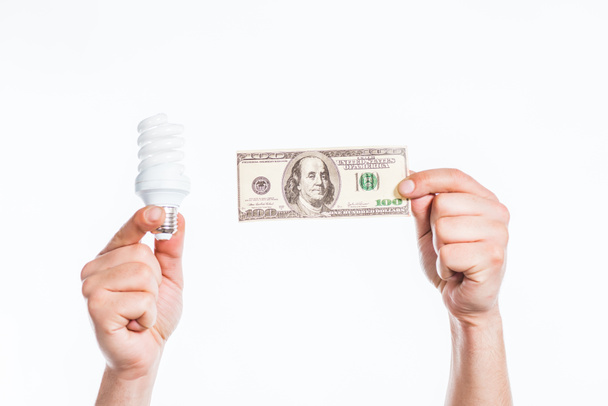 Erkek kırpılmış görünümünü holding floresan lamba eller ve yüz dolarlık banknot üzerinde izole beyaz, enerji verimliliği kavramı eller - Fotoğraf, Görsel