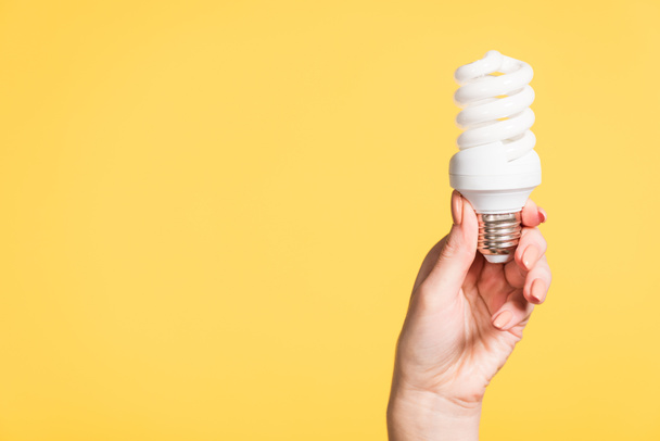 vista recortada de la lámpara fluorescente de mano femenina aislada en amarillo, concepto de eficiencia energética
 - Foto, imagen