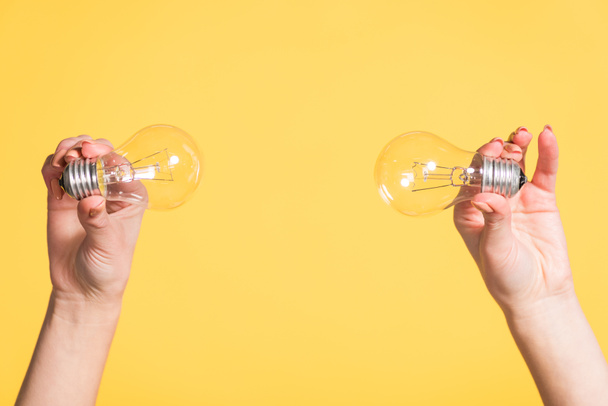 vista recortada de manos femeninas sosteniendo lámparas led aisladas en amarillo, concepto de eficiencia energética
 - Foto, Imagen