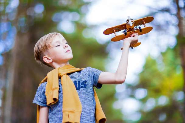 Przystojny chłopiec bawi się żółty samolocikiem na zewnątrz. Marzenia o podróży - Zdjęcie, obraz