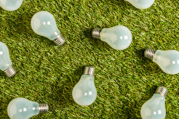 Blick von oben auf moderne Leuchtstofflampen auf grünem Gras, Energieeffizienzkonzept - Foto, Bild