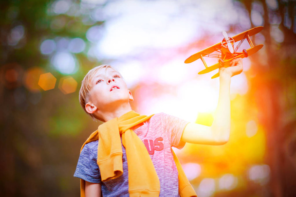 Handsome boy playing with yellow toy airplane outdoors. Dreams of traveling - Fotografie, Obrázek