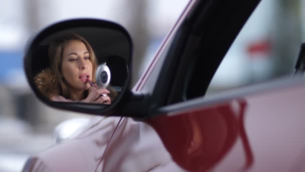 Mooi meisje in de auto schildert lippen met roze lippenstift. Reflectie in de spiegel, kant 4k Slow-Mo - Video