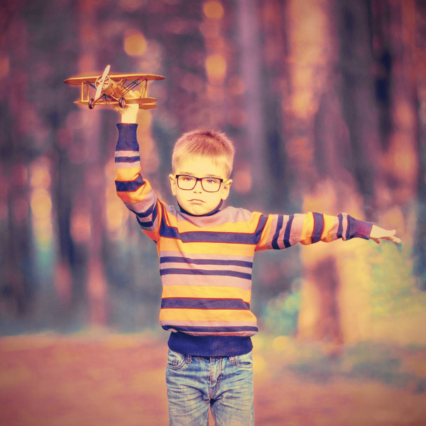 Divertido niño pequeño con gafas jugando con el avión de juguete al aire libre. Sueños de viajar
 - Foto, imagen