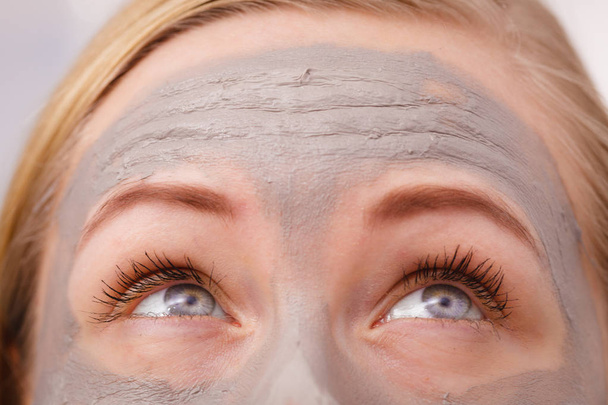 Facial dry skin and body care, complexion treatment at home concept. Closeup of woman having grey mud mask on face, eyes looking up above. - 写真・画像