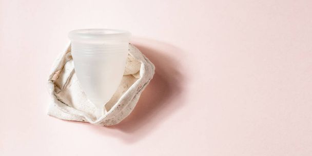 Copo menstrual em saco de algodão sobre fundo rosa. Alternativa ambientalmente amigável produto de higiene feminina. Conceito de saúde da mulher
 - Foto, Imagem
