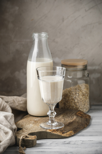 Niet-zuivel haver melk voor veganistisch dieet. Haver vlokken in glazen pot en glazen fles melk op rustieke achtergrond - Foto, afbeelding