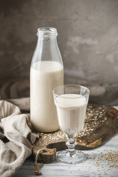 Немолочне вівсяне молоко для веганської дієти. Скляна пляшка молока і вівсяних пластівців, розкиданих на сільському столі
 - Фото, зображення