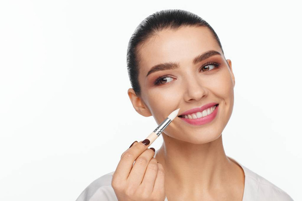 Portrait of a beautiful smiling young woman holding in her hand a white brush for makeup correction. White background - Foto, Imagem