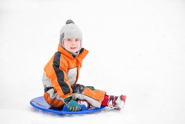 Mały chłopiec slajdy w dół wzgórza na śniegu spodek. Koncepcja sezonowe. Zimowy dzień. - Zdjęcie, obraz
