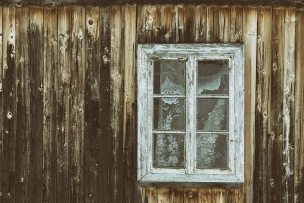 Vintage wooden window in a wall of shabby dark wooden boards with knots. Frontal view. Close-up - Photo, Image