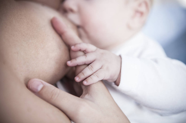 Niño pequeño agarra su dedo blanco madre que está amamantando. Primer plano.
 - Foto, imagen