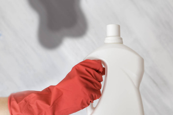 Gloved hand holding a bottle of washing liquid. Spot on background - Φωτογραφία, εικόνα
