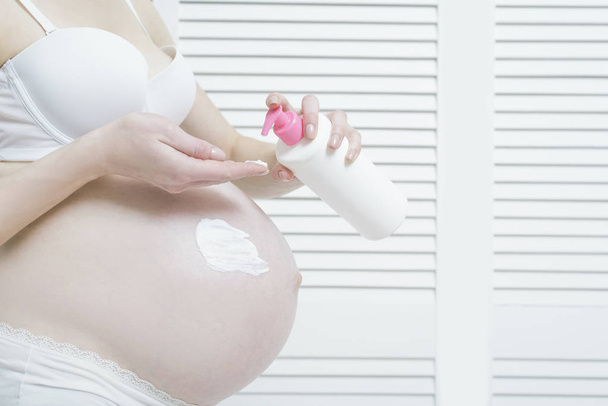 Έγκυος γυναίκα εφαρμόζεται κρέμα στην κοιλιά της. Γκρο πλαν - Φωτογραφία, εικόνα