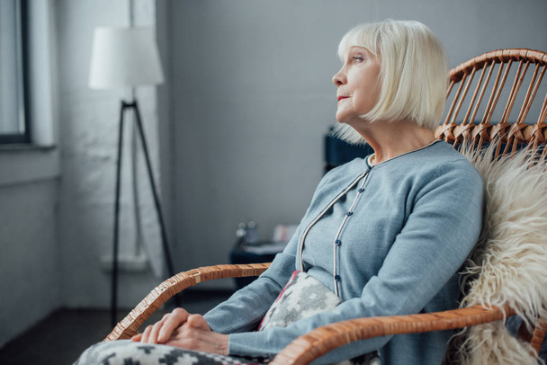 senior woman sitting in wicker rocking chair at home and looking away - Valokuva, kuva