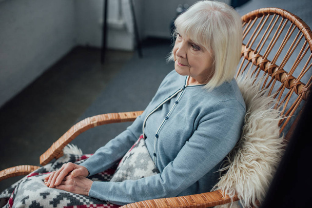 sad senior woman sitting in wicker rocking chair at home - Foto, Imagen