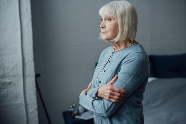 pensive senior woman in casual sweater with arms crossed at home - Photo, Image