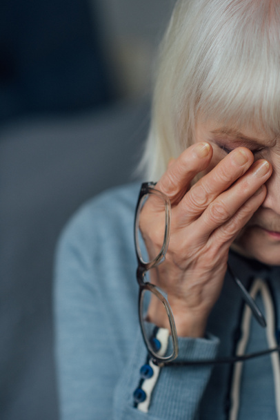 Senior vrouw met glazen en grijs haar veegde tranen en huilen thuis - Foto, afbeelding