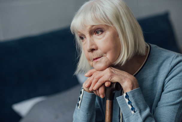 portrait of thoughtful senior woman with hands on walking stick sitting on bed at home - Foto, imagen