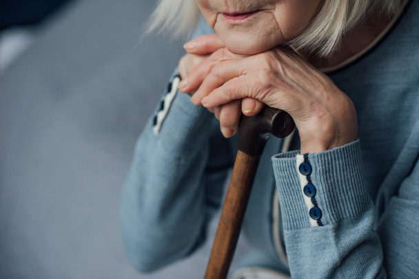 cropped view of senior woman with hands on walking stick sitting on bed at home - Foto, imagen