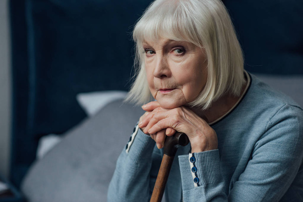 pensosa donna anziana con le mani sul bastone da passeggio seduto sul letto a casa e guardando la fotocamera
 - Foto, immagini