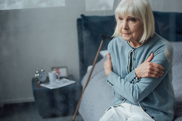 donna anziana sola seduta sul letto con le mani incrociate a casa
 - Foto, immagini
