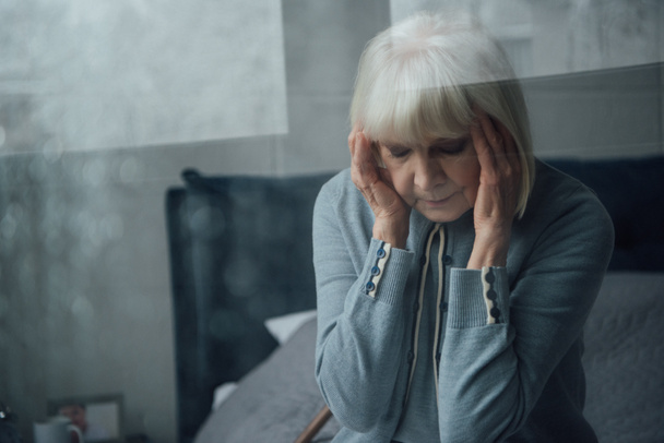 senior woman with hands on head sitting on bed and having headache at home  - Valokuva, kuva