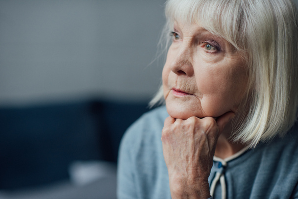 portrait of thoughtful senior woman propping chin with hand at home - Photo, Image