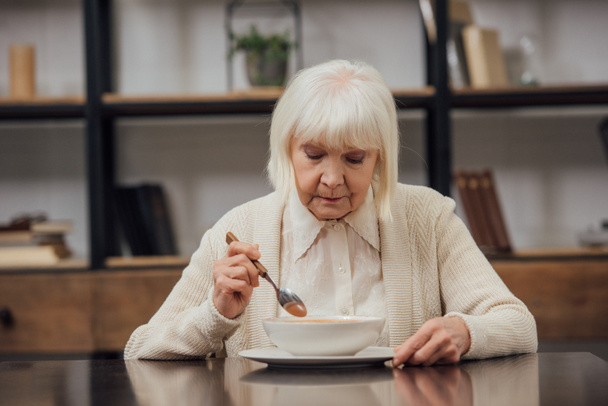 triste anciana solitaria sentada en la mesa y comiendo en casa
 - Foto, Imagen