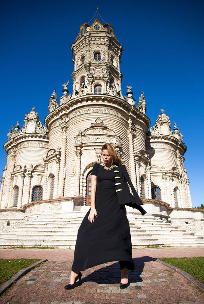 Young beautiful woman in black dress on the background of the church - Фото, изображение