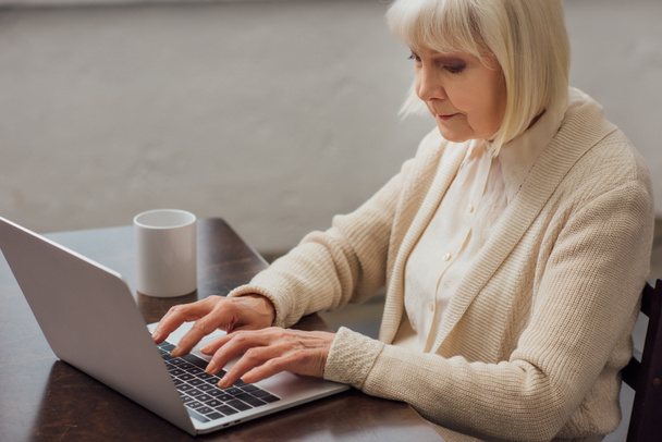 donna anziana seduta a tavola e digitando sul computer portatile a casa
 - Foto, immagini